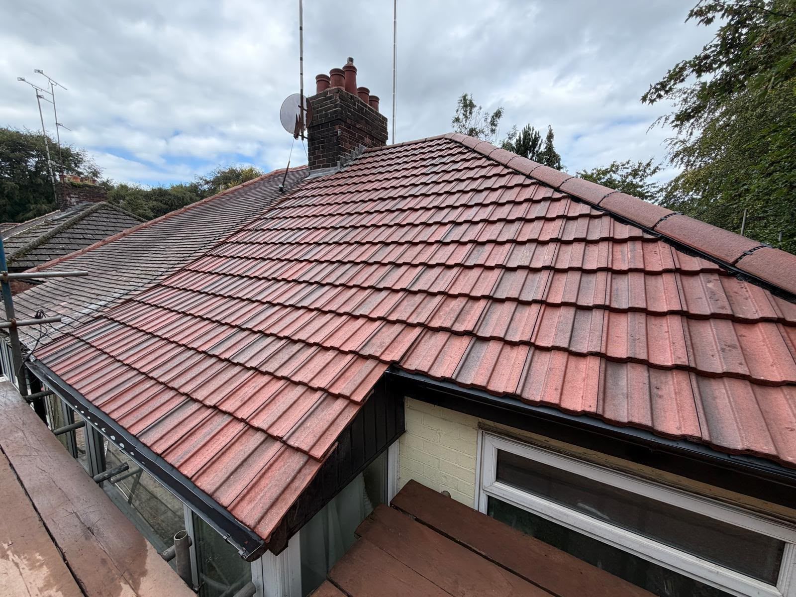 Red tiled roof with chimney on a house under a cloudy sky