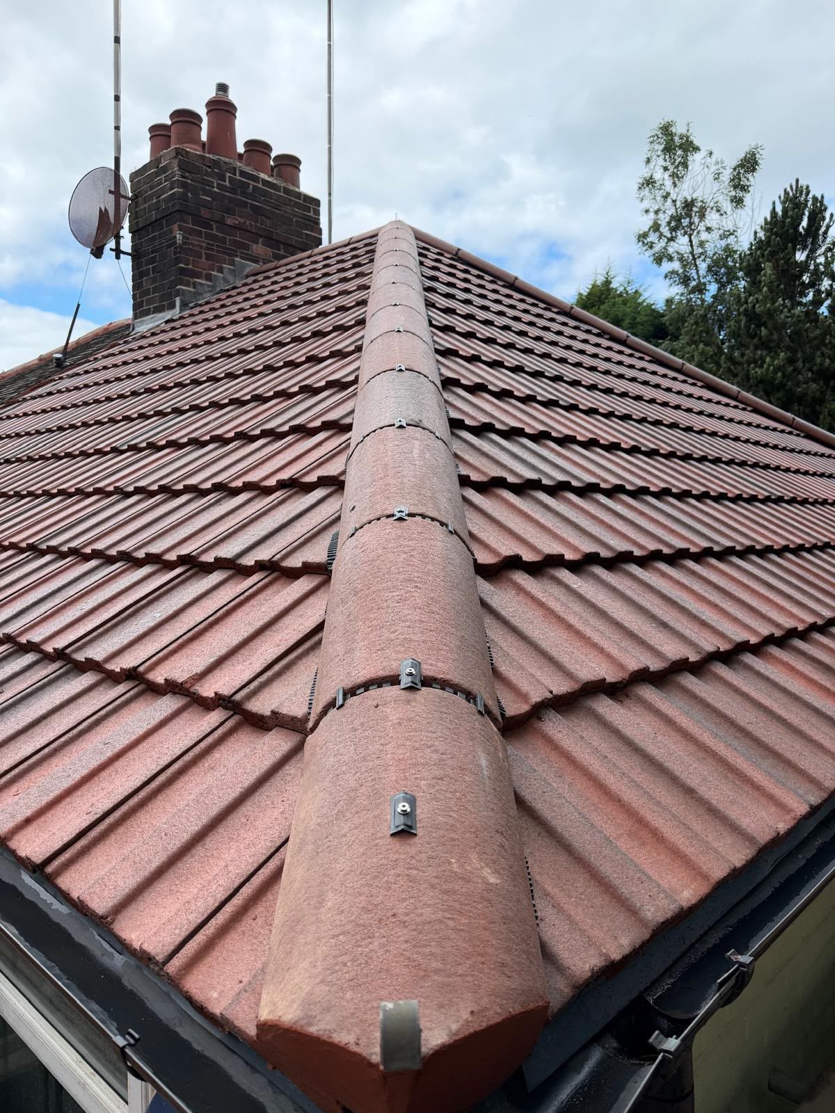 Red tiled roof with a central ridge vent and chimney under a cloudy sky