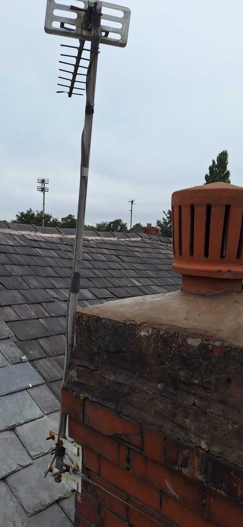Rooftop with brick chimney and TV antenna against a cloudy sky