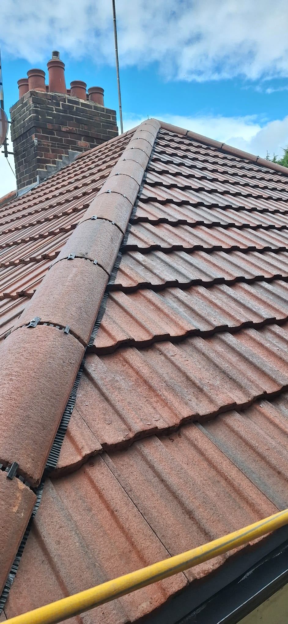 Roofer’s view of a tiled house roof with a brick chimney under a blue sky