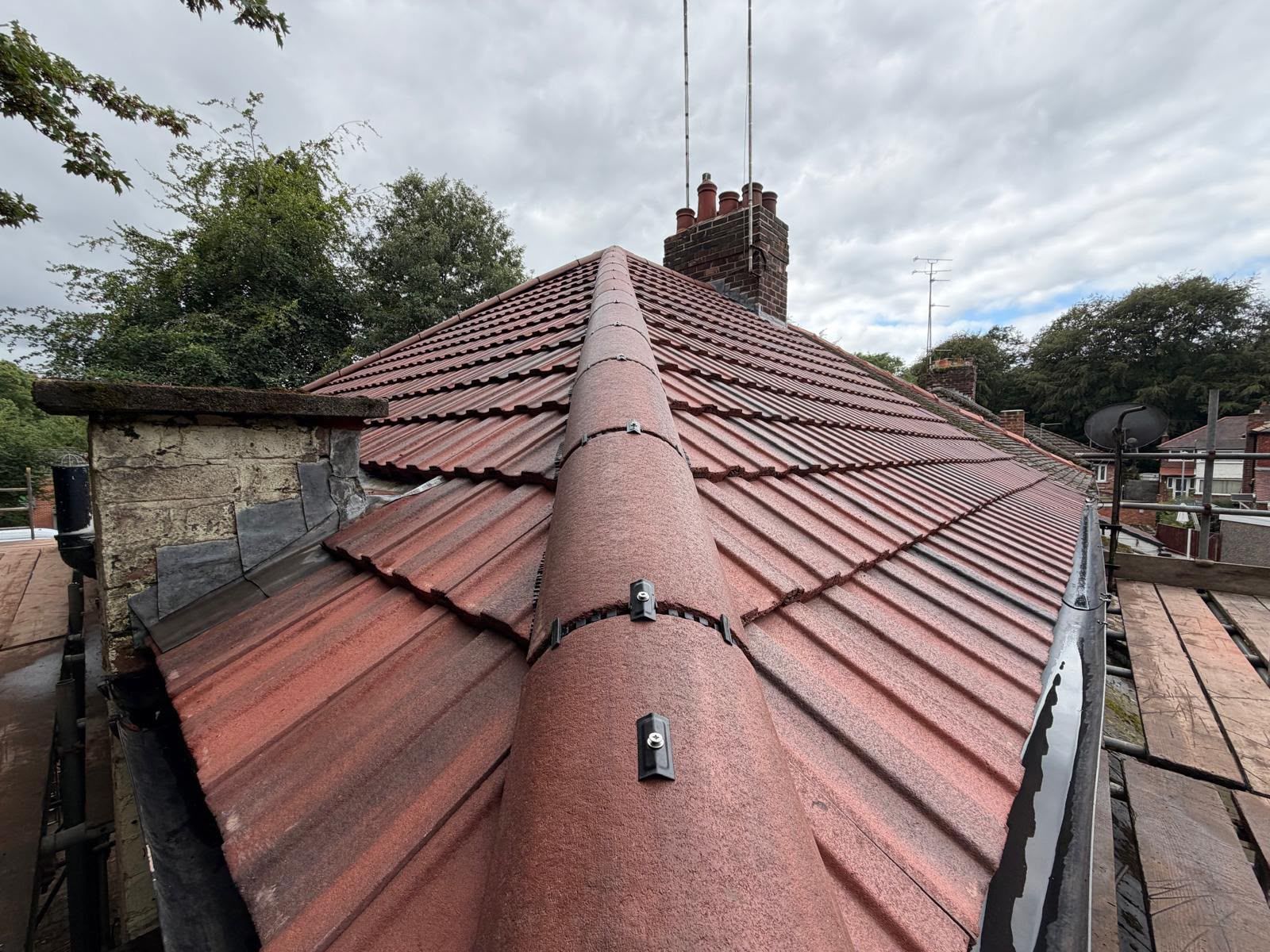 Rooftop with red clay tiles and central ridge vent under an overcast sky