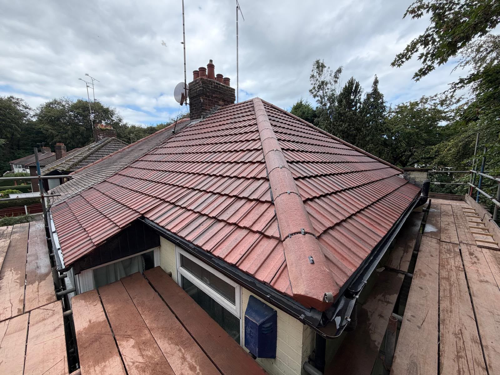 Red-tiled roof on a house under cloudy skies, with trees surrounding it.