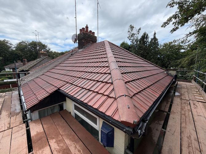 House roof with reddish-brown shingles and chimneys, viewed from above under a cloudy sky