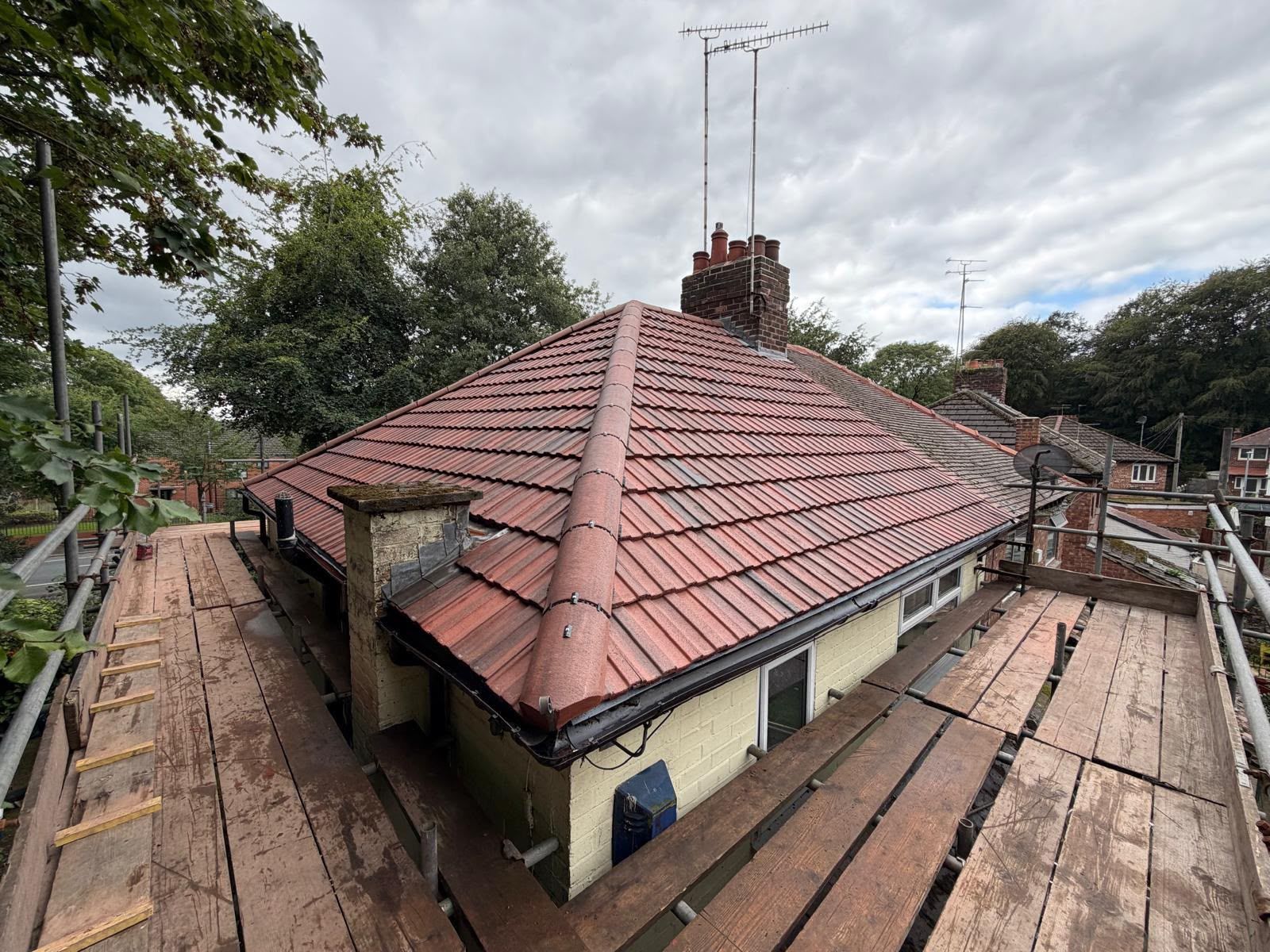 Rooftop with red tiles and a central brick chimney on a house under cloudy skies