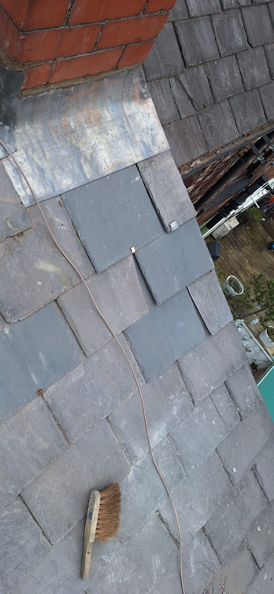 Tilted view of a gray slate roof with a brick wall, patch repair, and a leaf on the surface