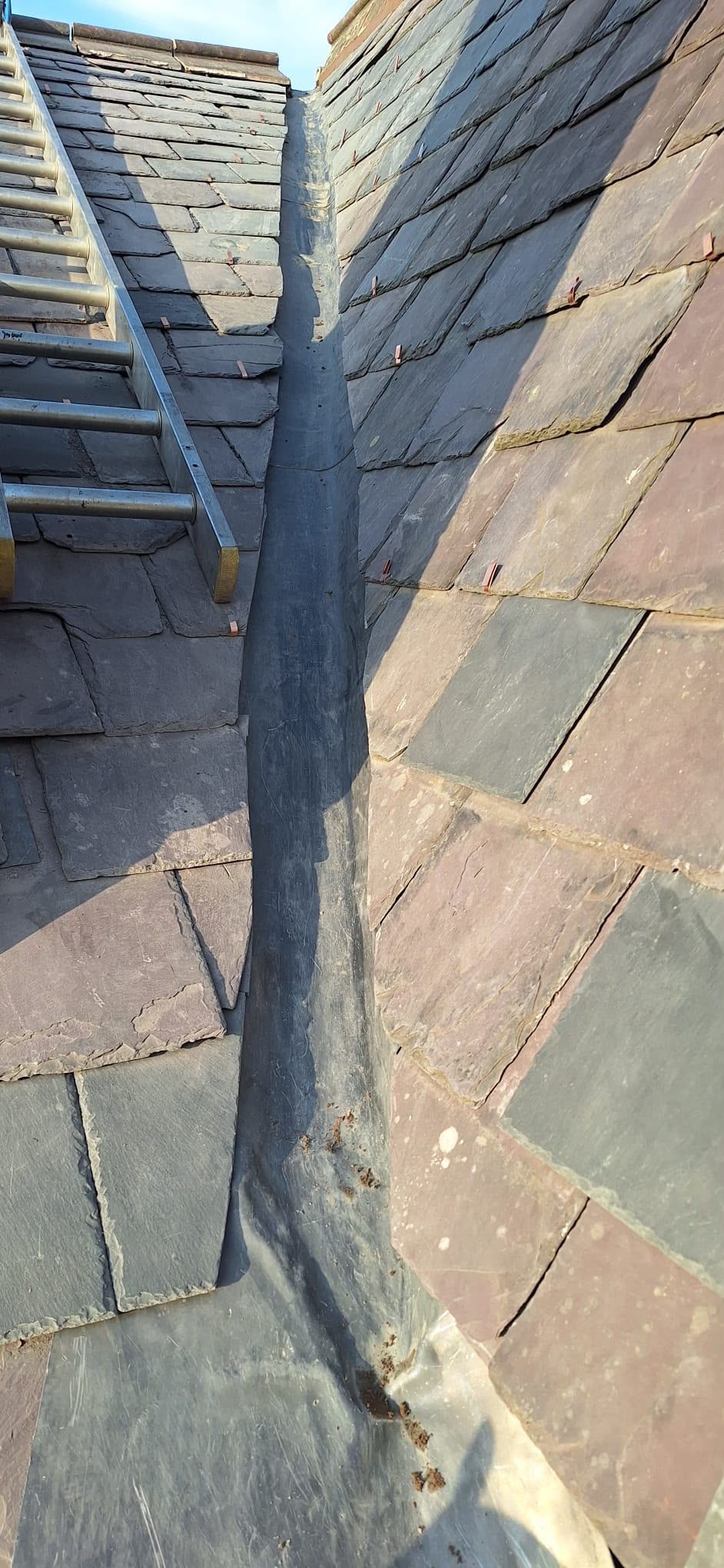 Close-up of a slate roof valley with gray shingles and a narrow gutter channel.