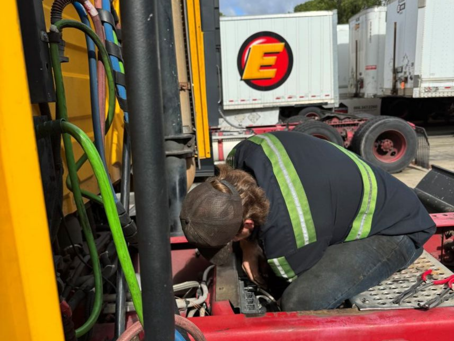 Mechanic working on the undercarriage of a yellow truck; outdoors.