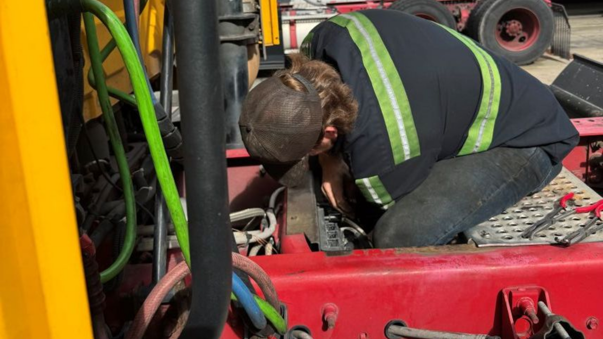 Mechanic working on the engine of a yellow and red truck, wearing a safety vest in Raleigh, NC.