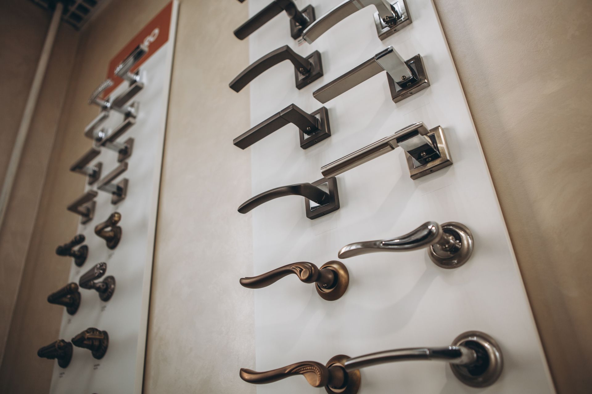 Display of various door handles in a store, mounted on white boards.