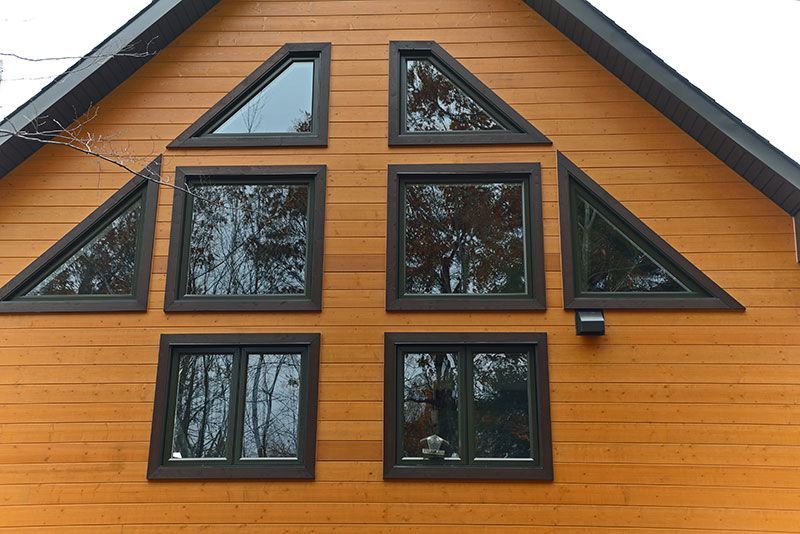 Maison orange en forme de A avec des fenêtres à cadre foncé de tailles variées, notamment triangulaires et carrées.