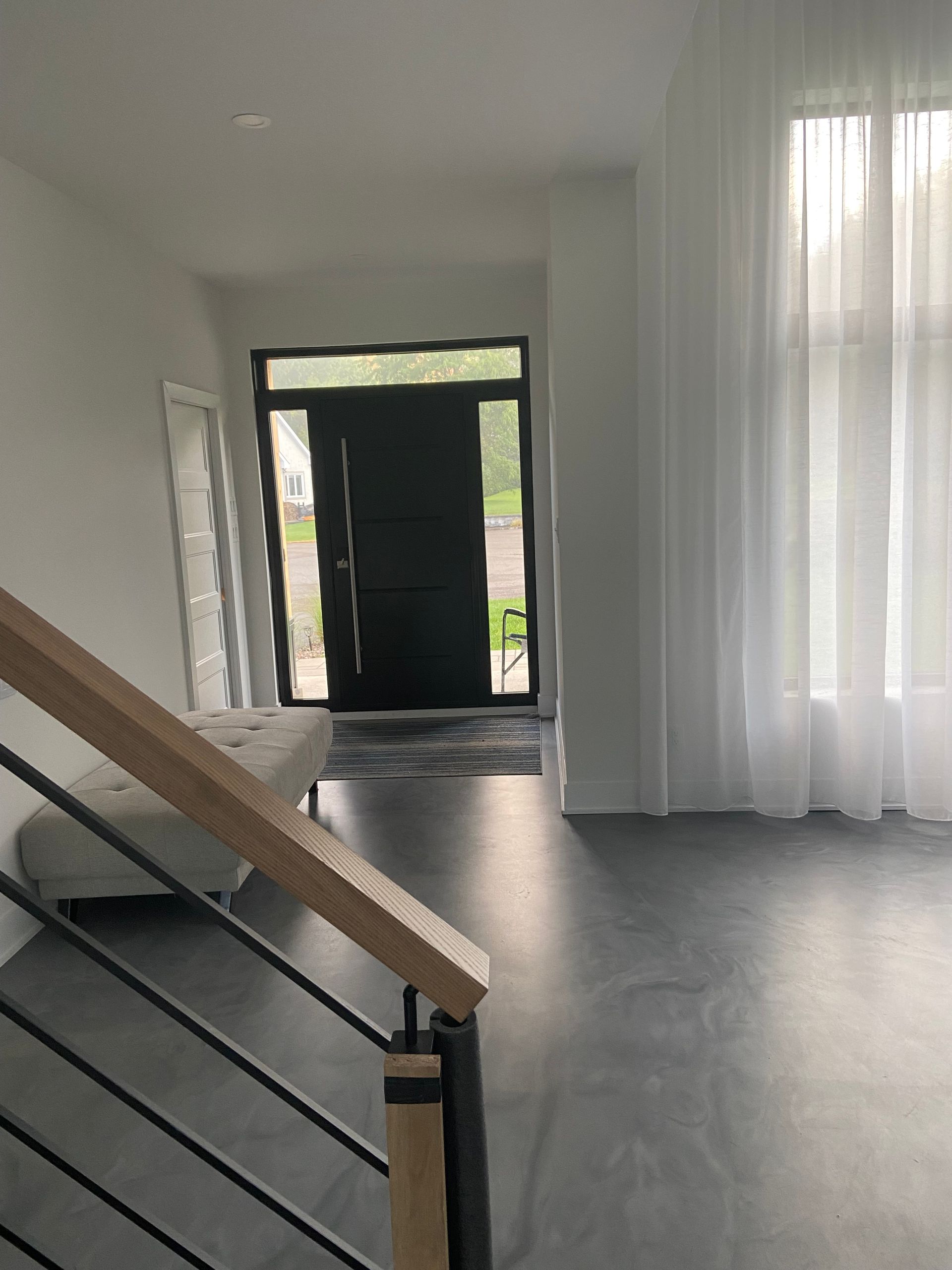 Entrée intérieure avec porte sombre, escalier avec rampe en bois et rideaux transparents.