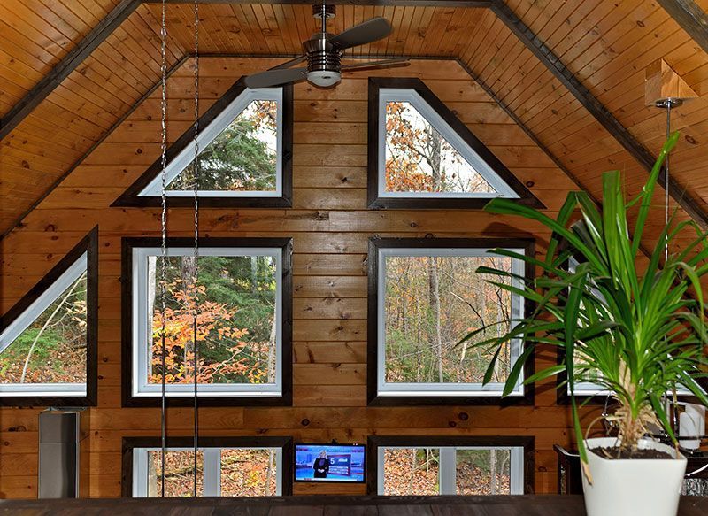 Intérieur lambrissé avec de nombreuses fenêtres encadrant le feuillage d'automne. Une plante se trouve à droite.