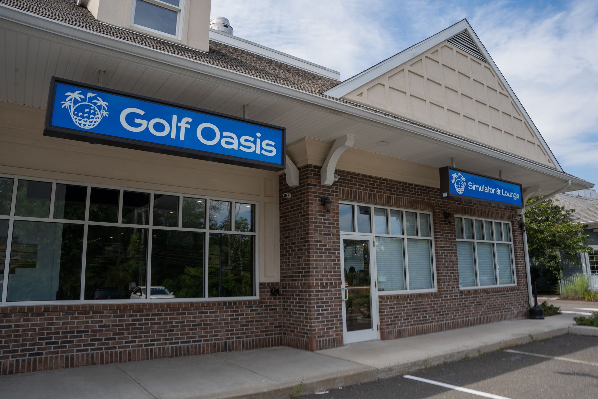 A storefront for Golf Oasis with large windows, brick siding, and a blue sign under an overhanging roof.