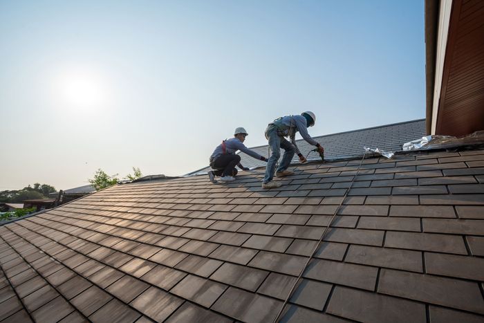 Two roofers working on a shingle roof in bright sunlight.