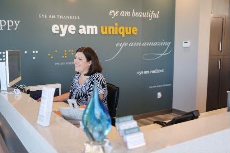 A woman is sitting at the front desk at Focal Pointe Eye Care in front of a wall that says eye am unique