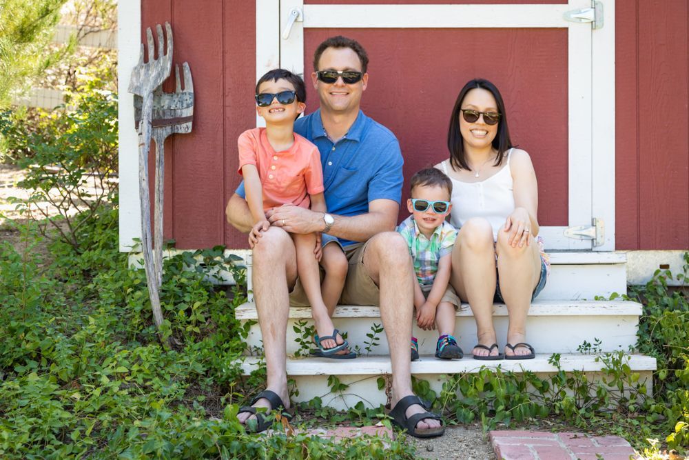 A family is sitting on the steps of a red shed wearing sunglasses