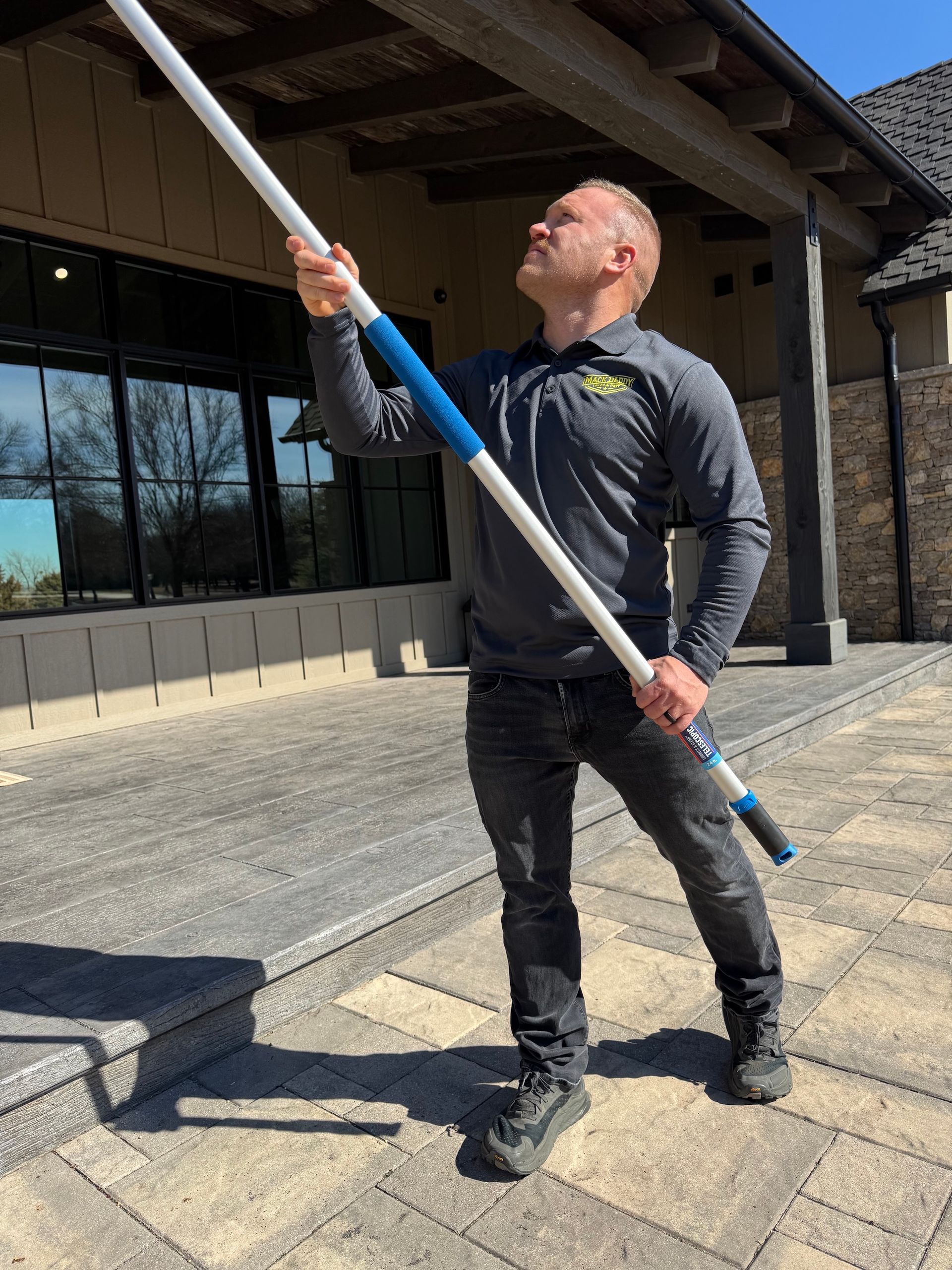 Man on a patio holds a long cleaning pole up to the underside of an awning.