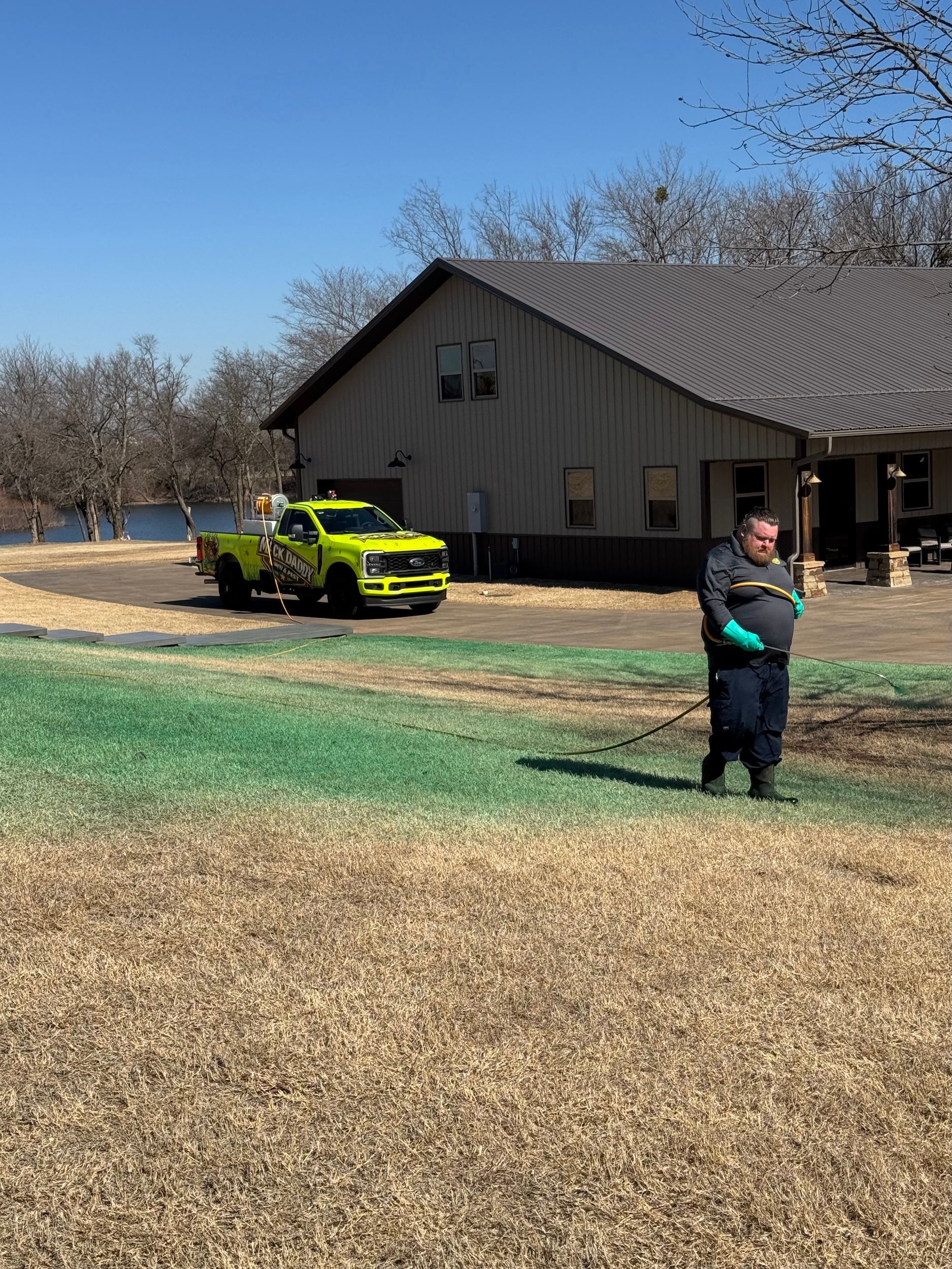 Man spraying in front of a building; a yellow truck is parked on the lawn.