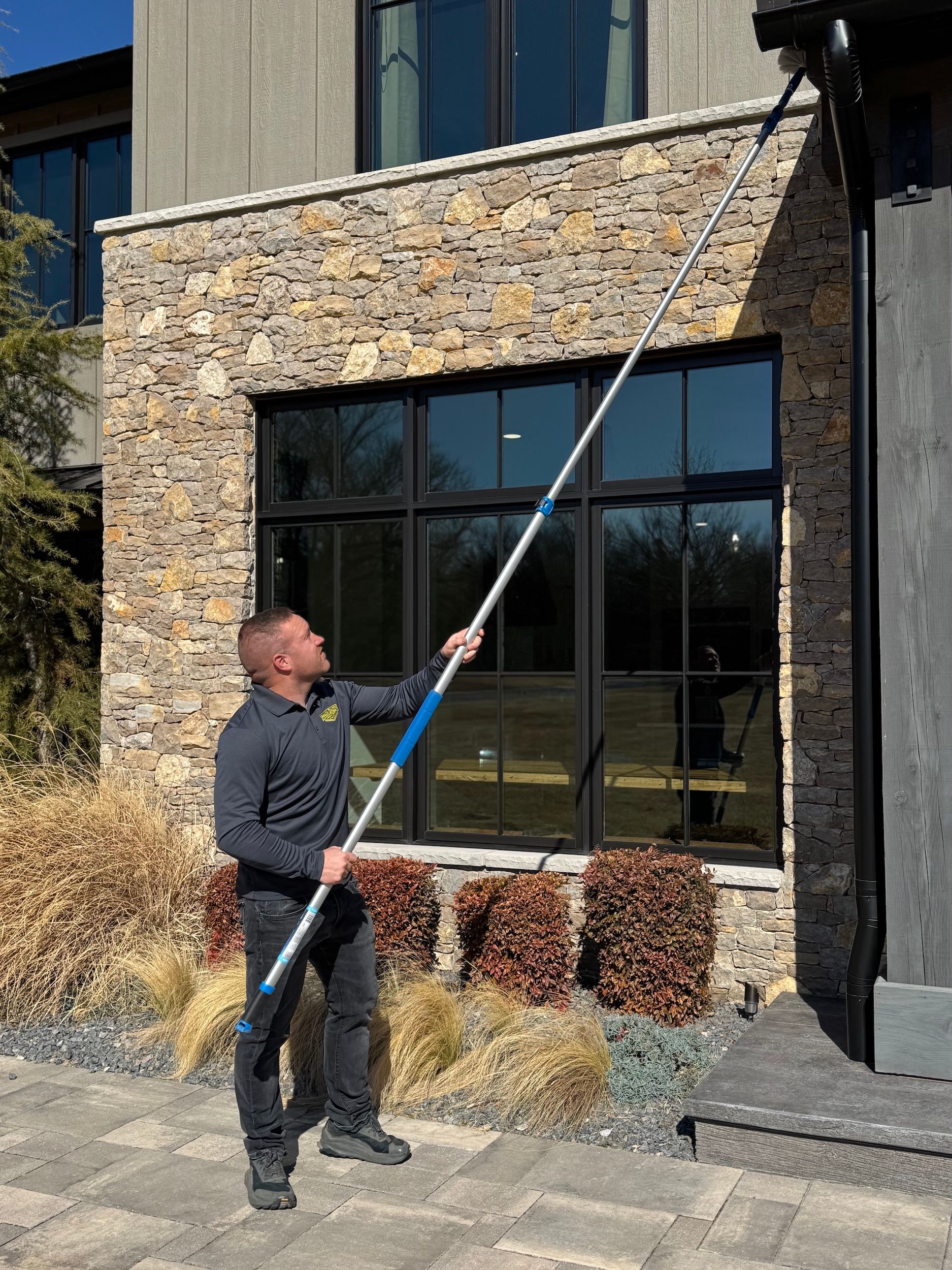 Man using a telescoping pole to clean a gutter on a stone-faced building.