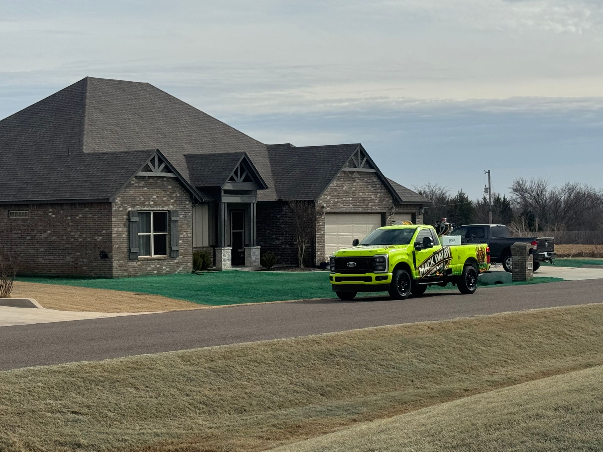 Lime green pickup truck parked in front of a brick house with a trailer attached, overcast day.
