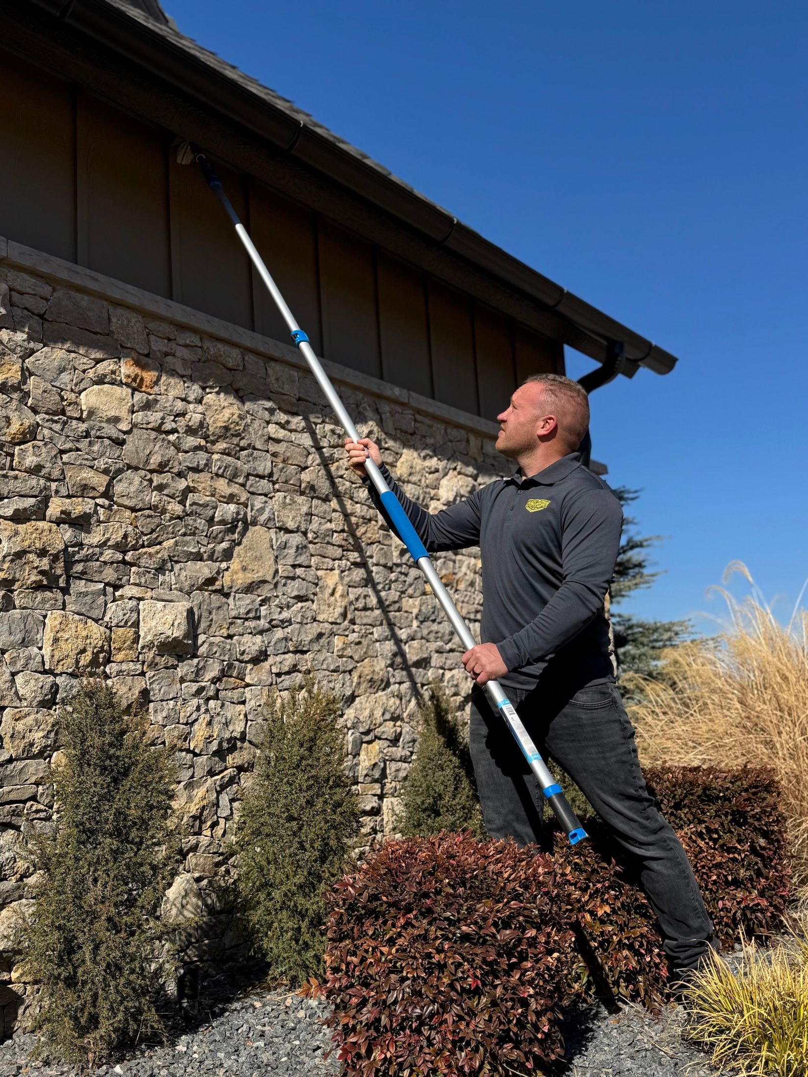 Person cleaning a house gutter with an extendable pole; outside on a sunny day.