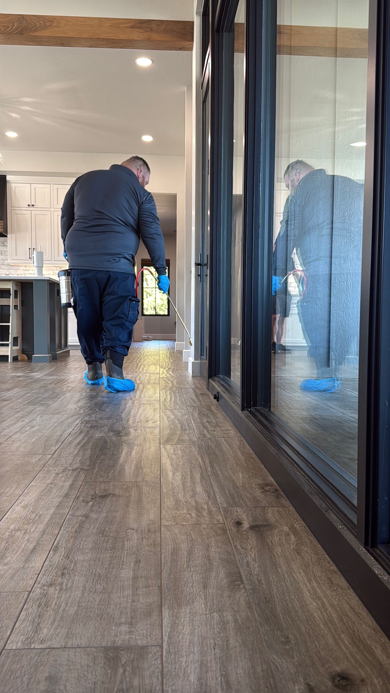 Person wearing blue shoe covers walking on a wood floor, reflected in a large window.