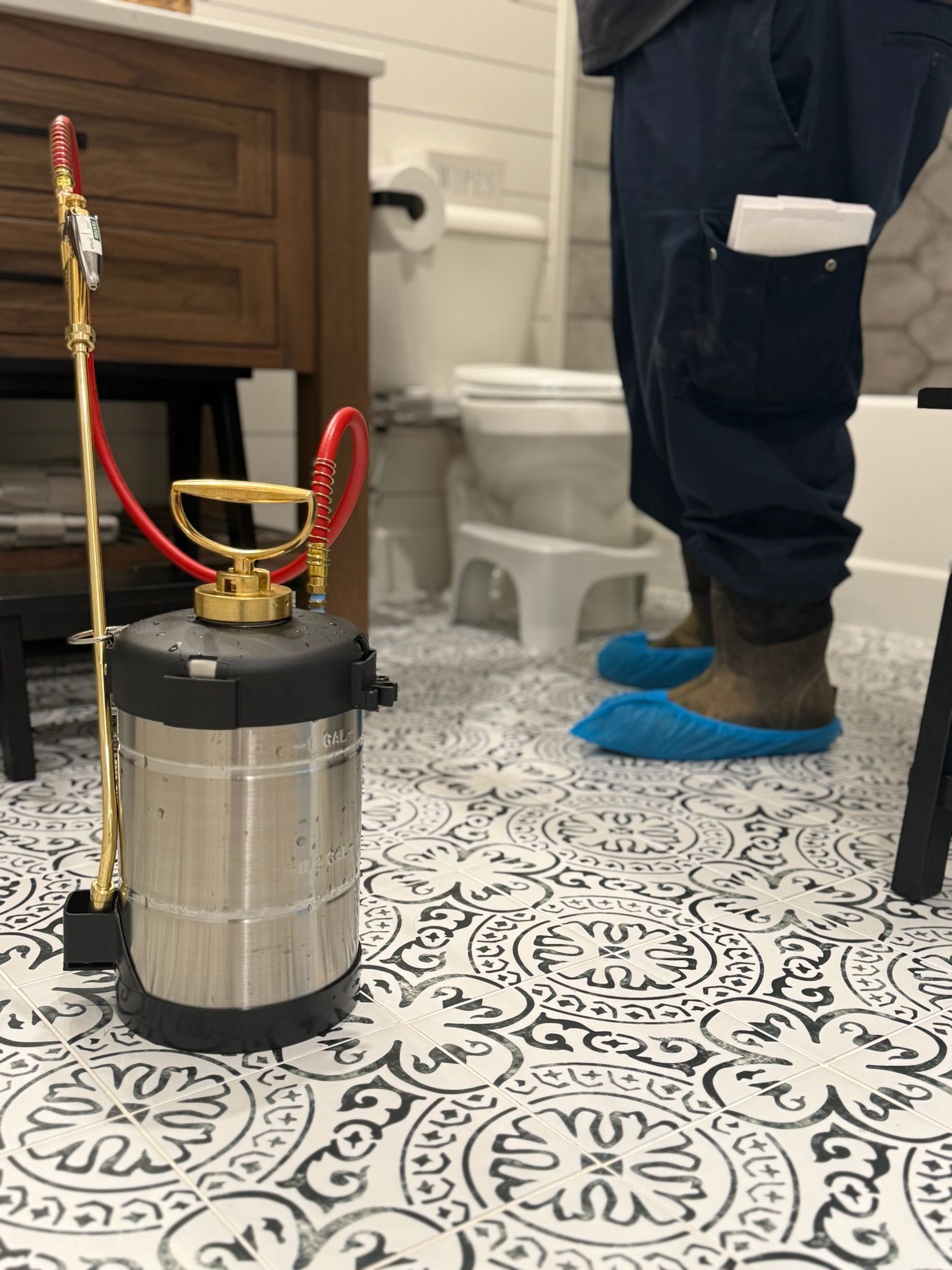 A person wearing blue shoe covers stands in a bathroom with a sprayer.
