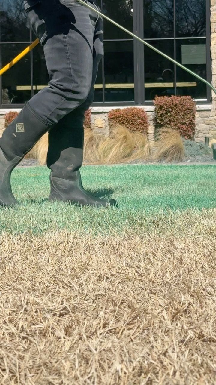 Person in rubber boots walks on grass, holding a long yellow pole with a wire.