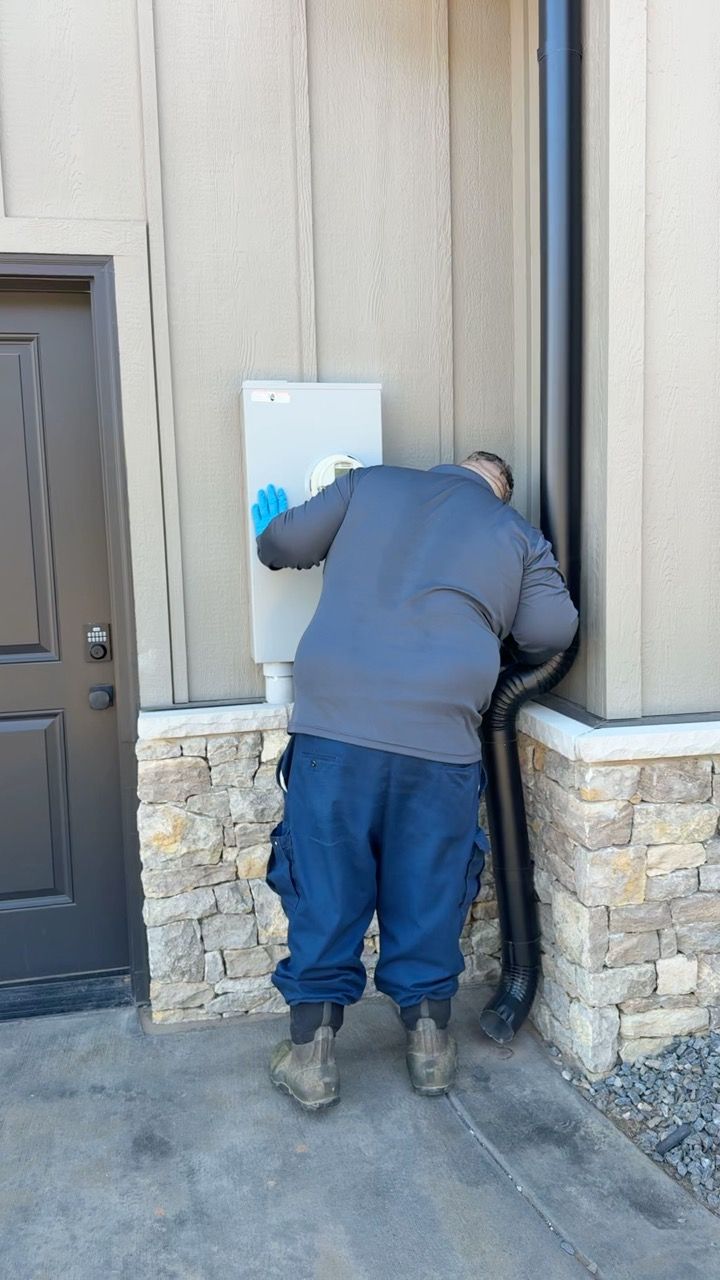 Person working on a white electrical box on the side of a building. He is wearing gloves and blue work pants.