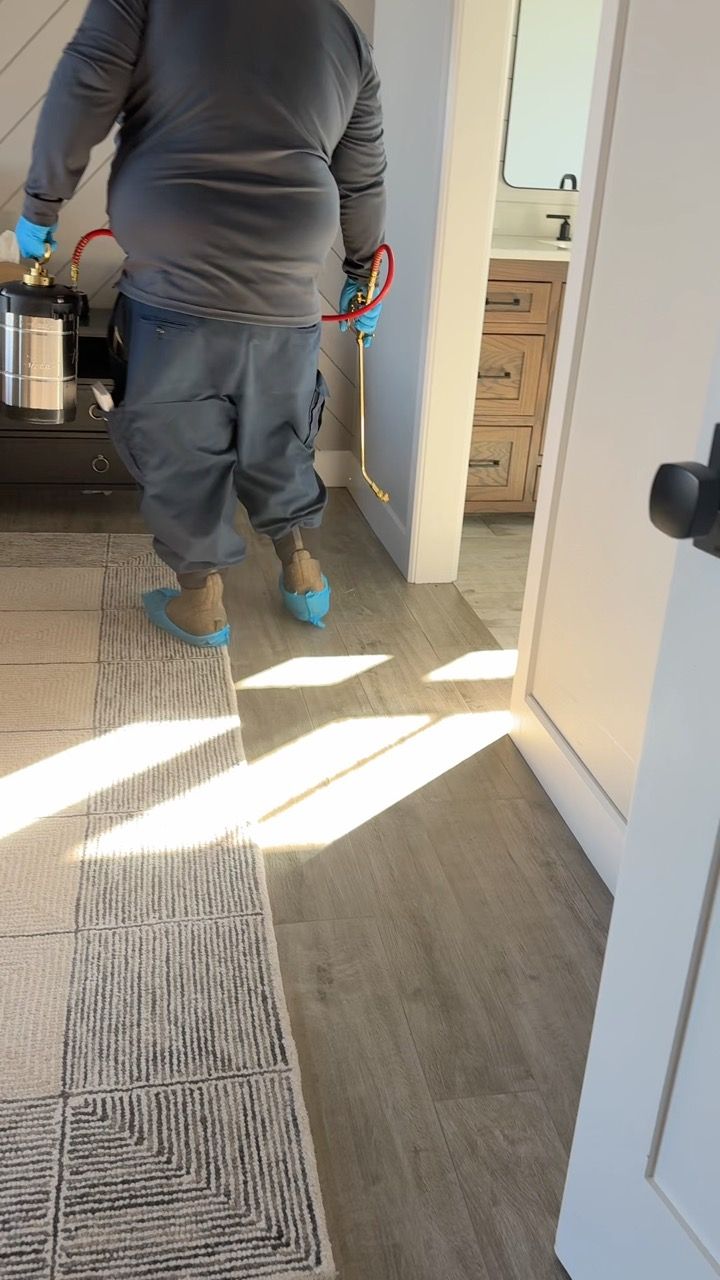 Person spraying disinfectant in a room, wearing protective gear.
