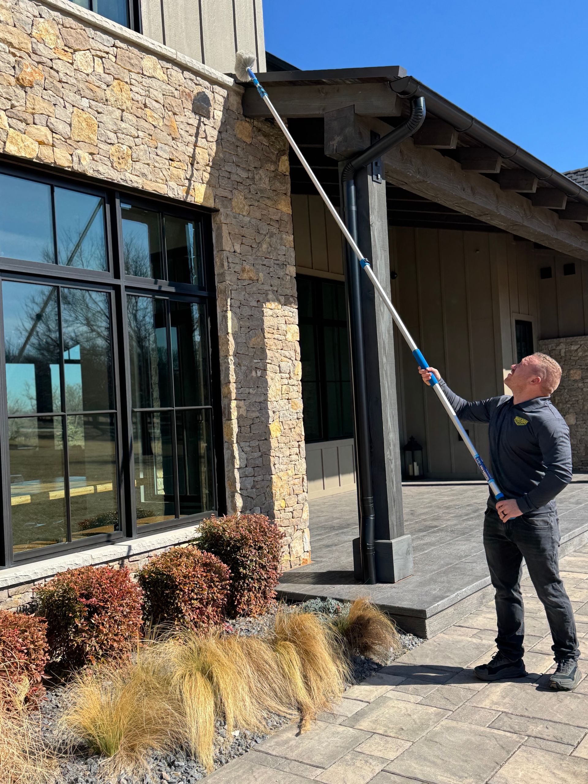 Man cleaning gutters of a house using a long-handled brush.