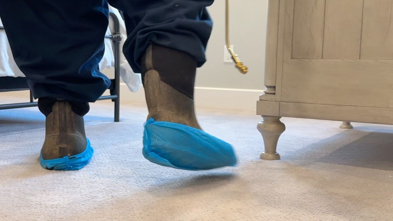 Person wearing blue shoe covers over boots, walking on carpet.