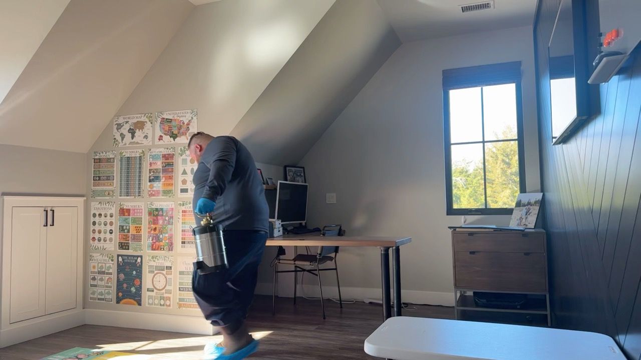 Person carrying a bucket in a room with a desk, window, and posters on the wall.