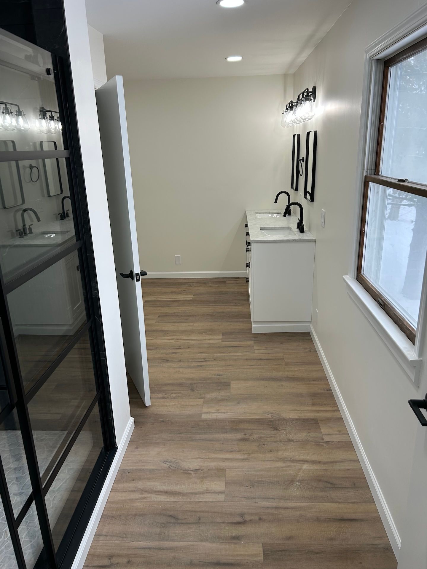 A hallway leading to a bathroom with two sinks and a window.