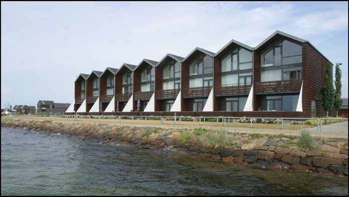 Række af moderne brune huse med trekantede tage langs en havnefront.