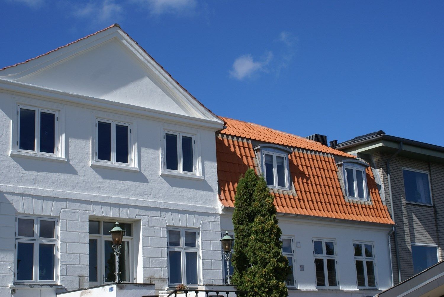 Hvid bygning med rødt tegltag, blå himmel i baggrunden.