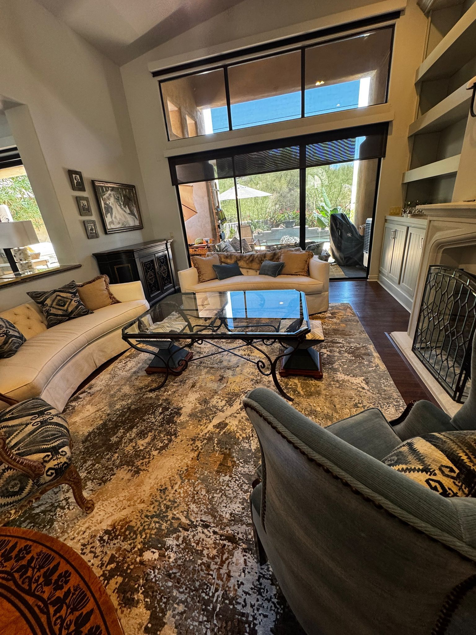 Modern living room with beige sofa, glass coffee table, patterned rug, and large windows overlooking greenery