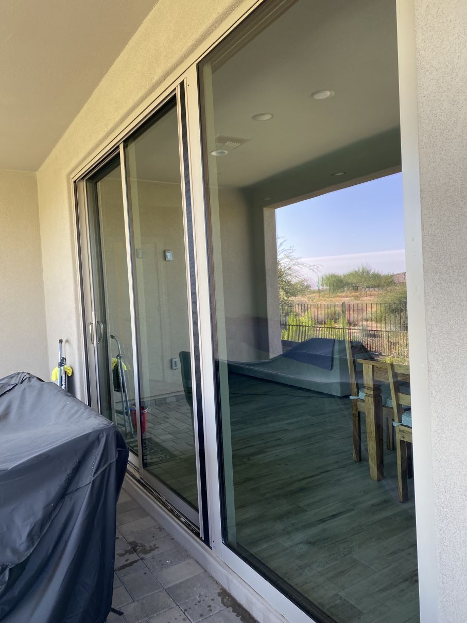 Sliding glass doors opening to a covered patio with a grill and outdoor seating reflected in the glass