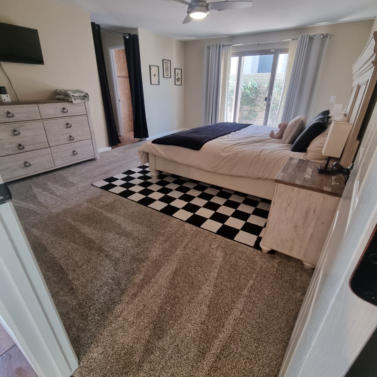 Spacious bedroom with a bed, black-and-white rug, dresser, and a window with curtains.