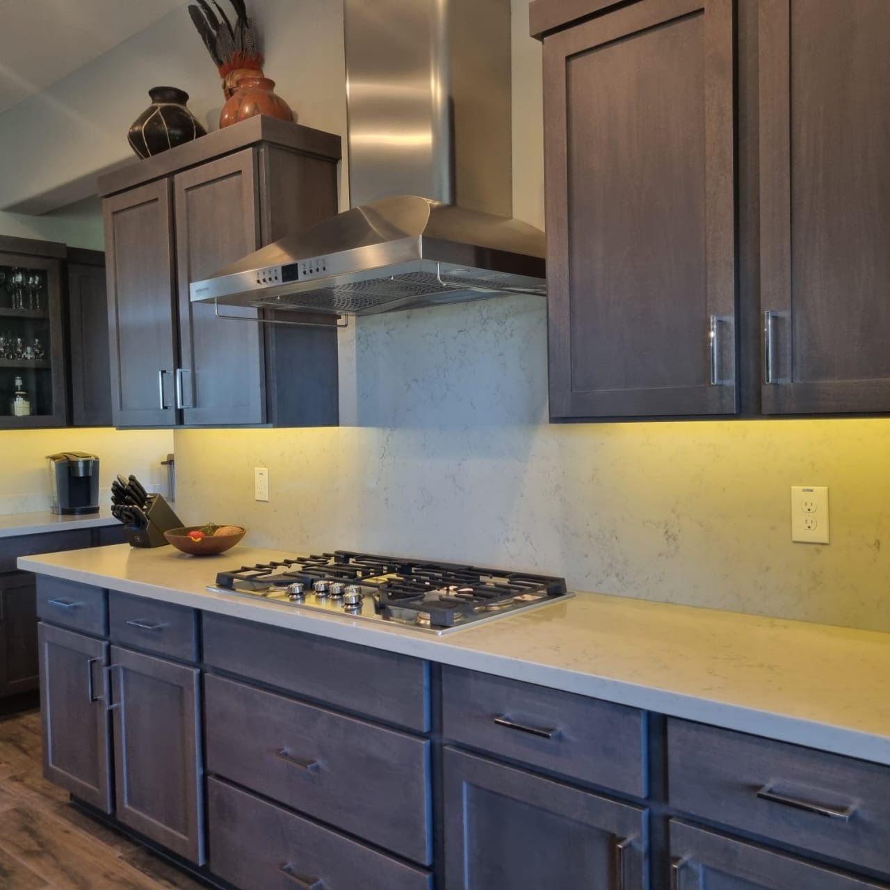 Modern kitchen with dark cabinets, light countertops, gas cooktop, and stainless steel range hood.