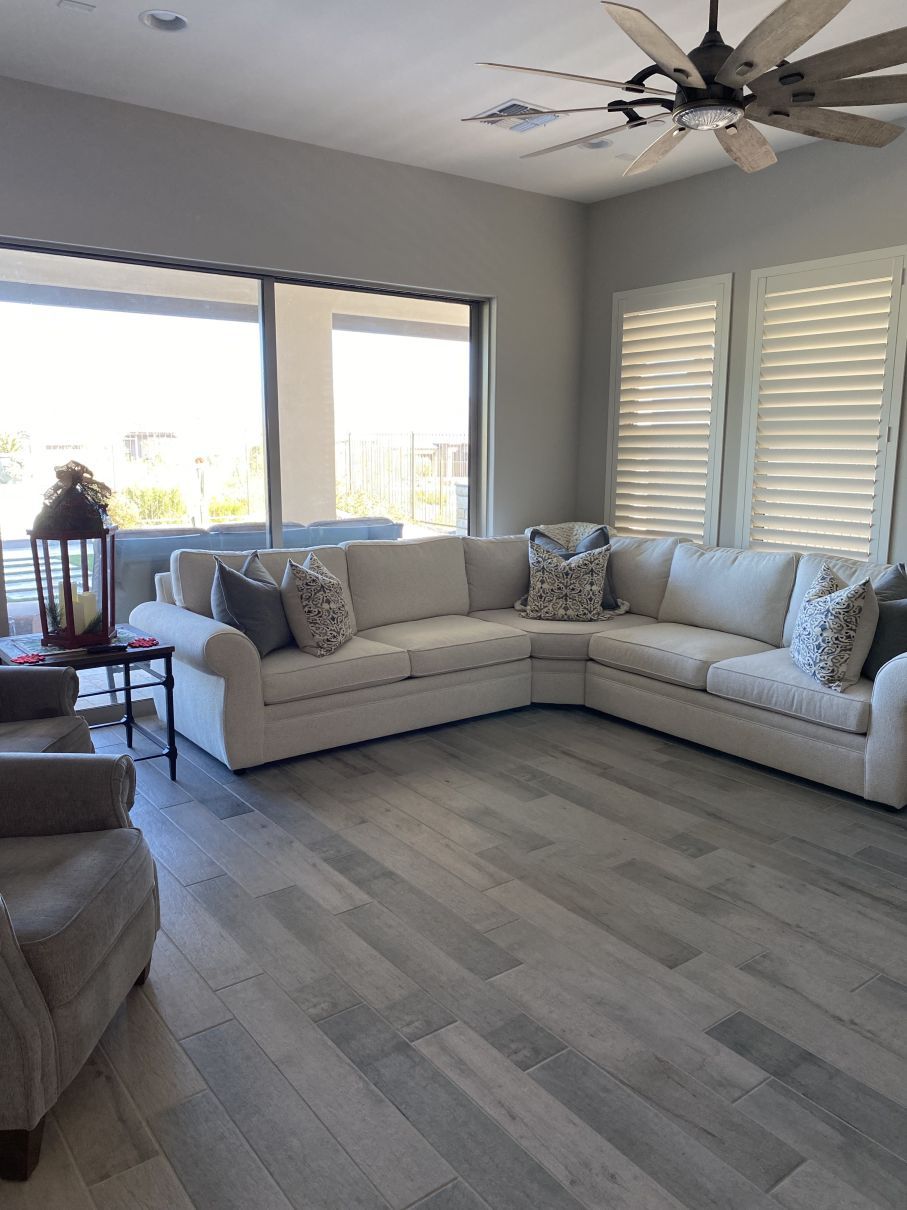 Bright living room with a large beige sectional, ceiling fan, gray wood floor, and sliding glass doors