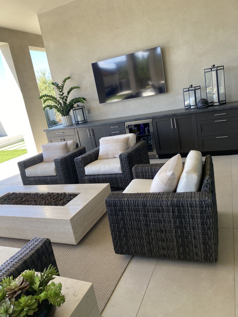 Modern outdoor patio with wicker lounge chairs, a coffee table, wall-mounted TV, and potted plants