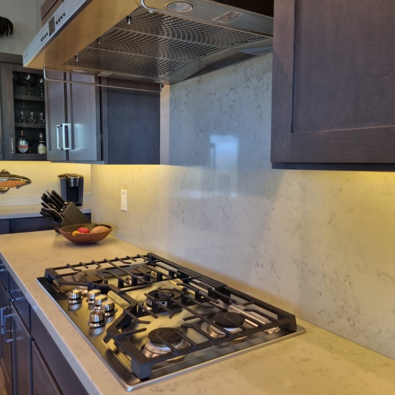 Modern kitchen with a gas cooktop, stainless hood, and light stone countertop on the left wall.