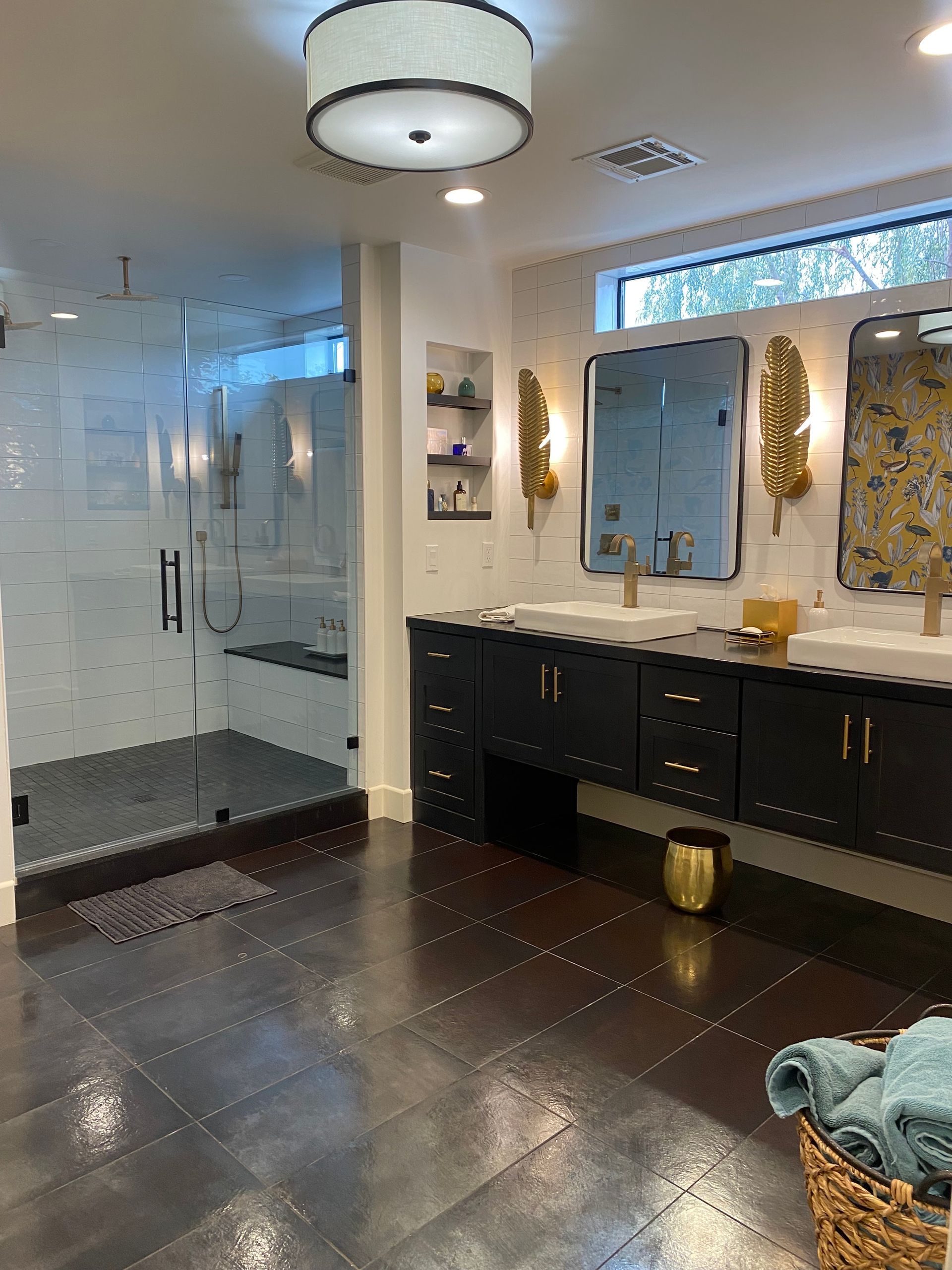 Modern bathroom with glass shower, dark vanity, large mirror, and brown tiled floor.