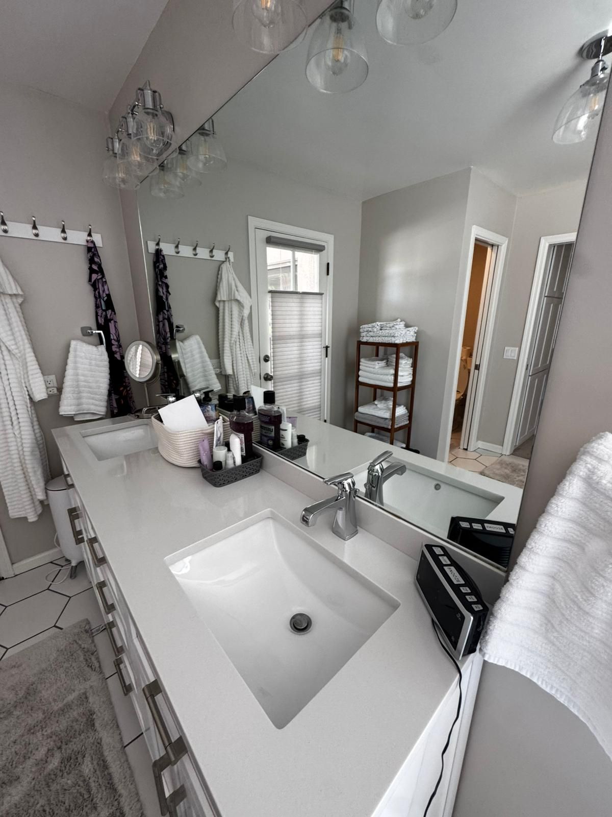Bright white bathroom with large vanity mirror, sink, shower curtain, and towel racks.