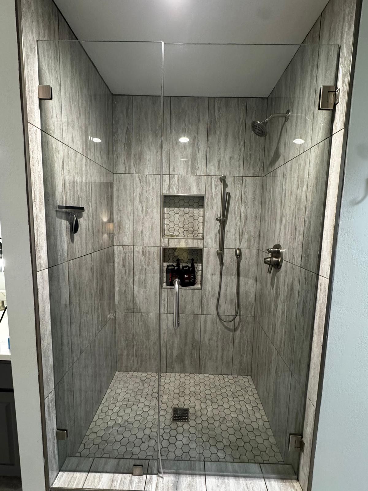 Walk-in shower with gray tile walls, glass door, bench, and built-in fixtures