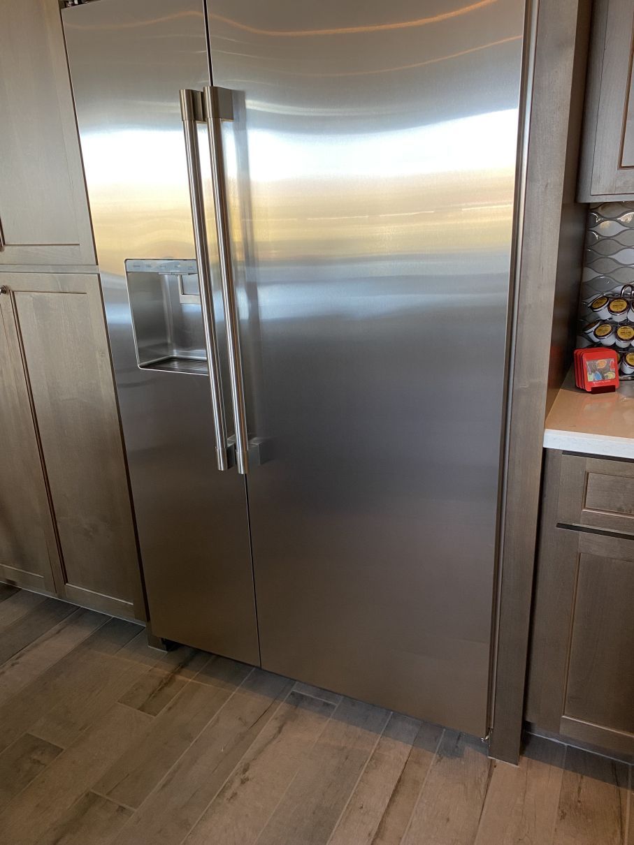 Stainless steel French-door refrigerator in a kitchen, with wood cabinets and a countertop beside it.