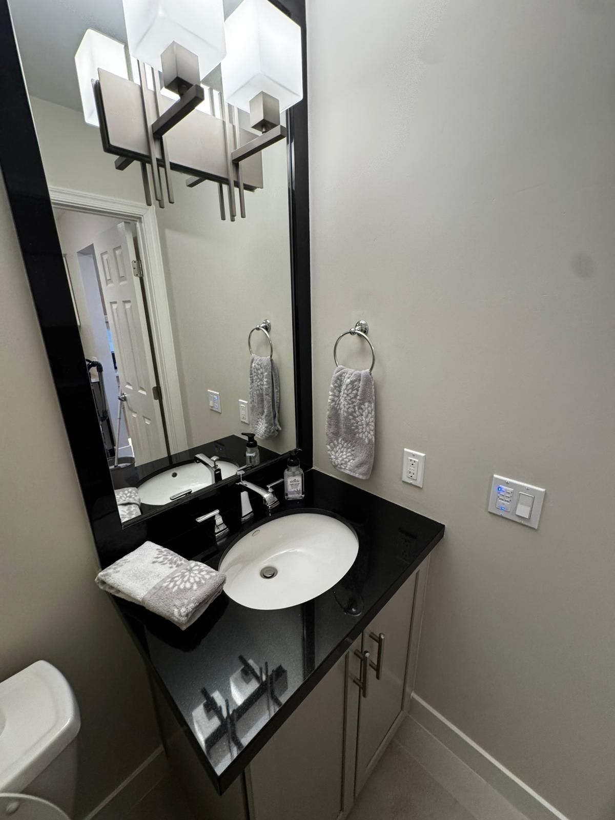 Small bathroom vanity with black counter, round sink, mirror, and wall sconces.