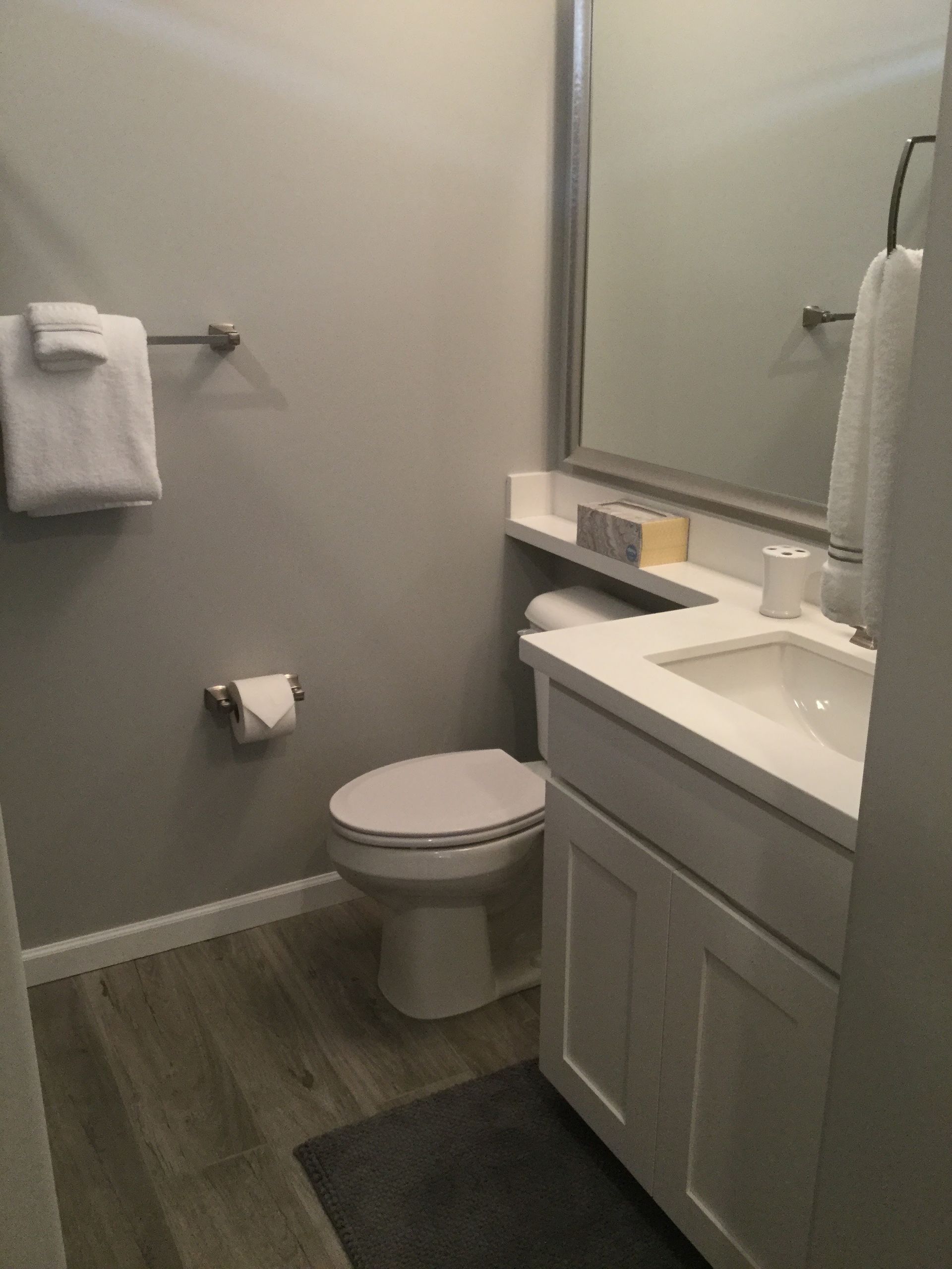 Small bathroom with toilet, sink vanity, towel rack, and dark floor mat.