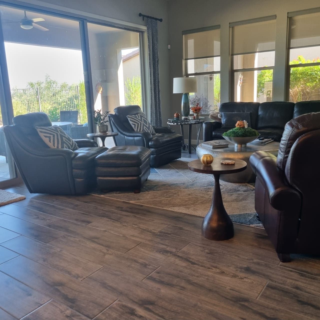 Modern living room with leather chairs, sofa, coffee table, rug, and large windows with sunlight